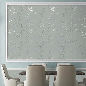 Grey-green cherry blossom branch print filling a wide white moulded rectangle on the wall above a dining table with four upholstered chairs