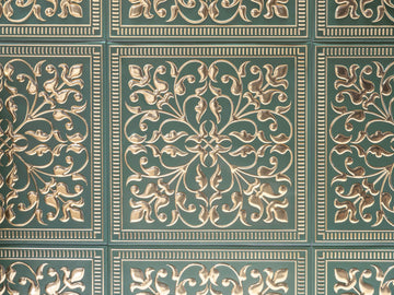 Close-up of embossed metal tiles with bright gold scrollwork and beaded borders pressed into a deep green ground, laid edge to edge in a grid