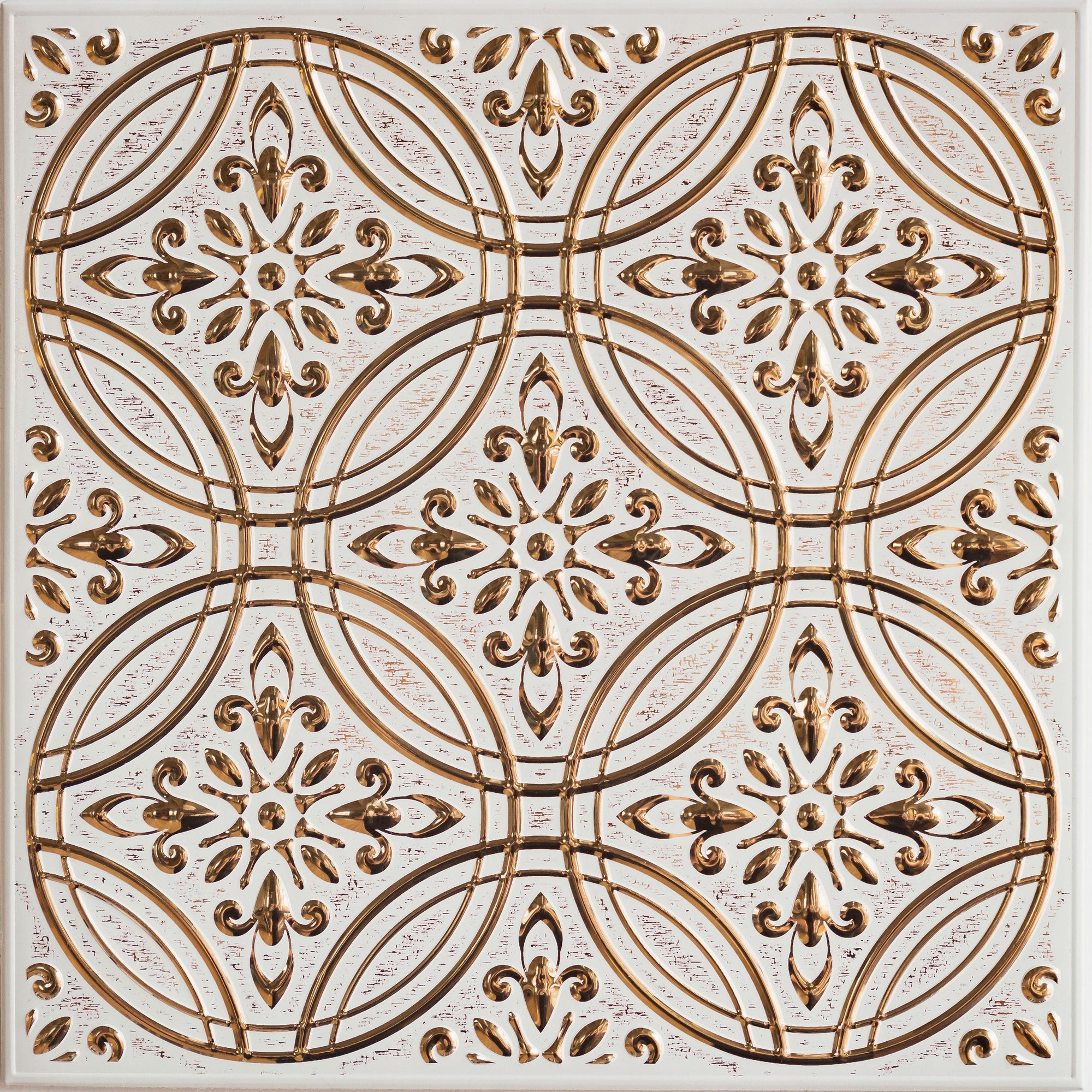 A single square peel and stick metal tile photographed straight on, its raised gold pattern of interlocking circles and fleur-de-lis motifs catching the light against a distressed off-white ground.
