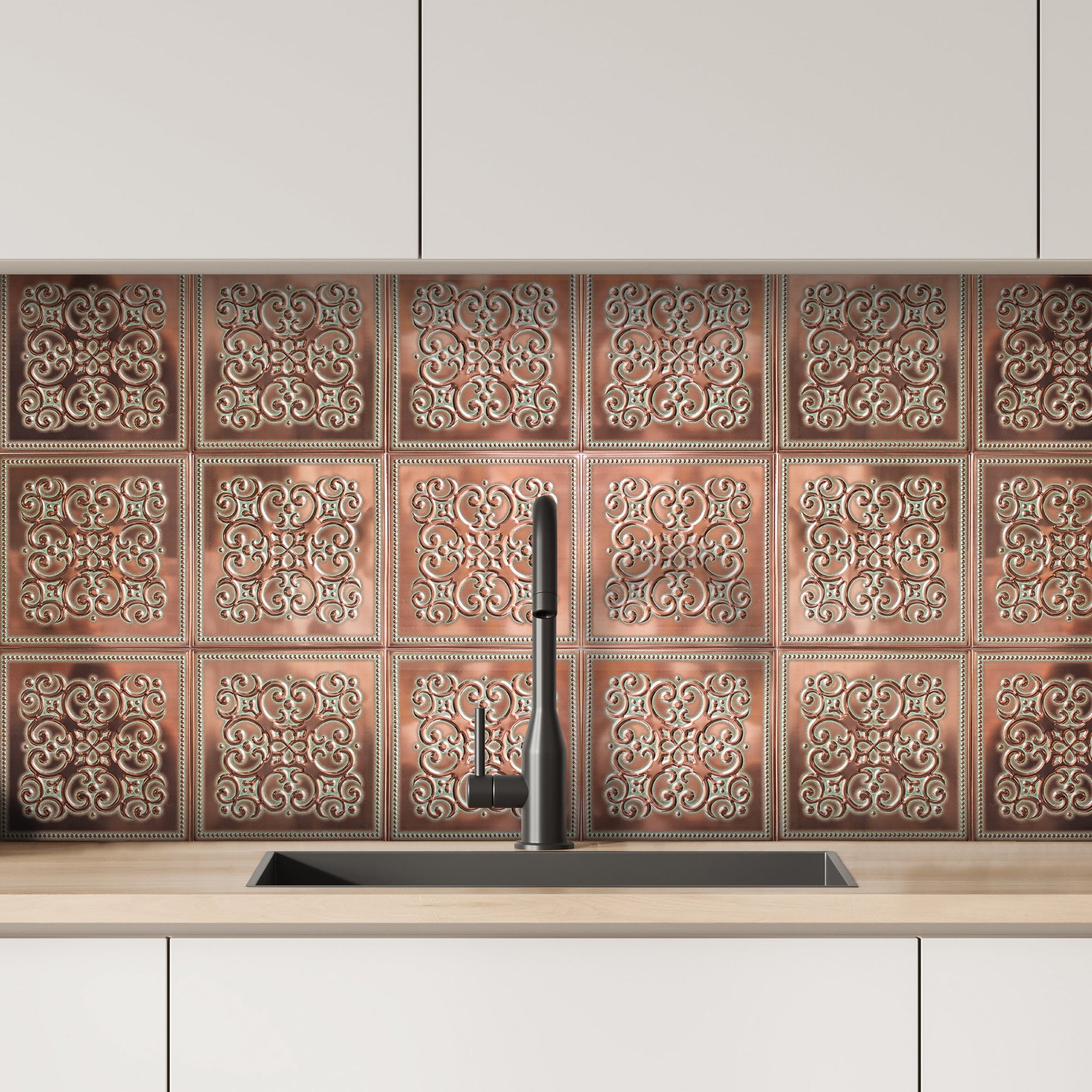 Copper-toned embossed metal tiles installed as a kitchen backsplash between white cabinets and a light wood countertop, with a black faucet over an undermount sink.
