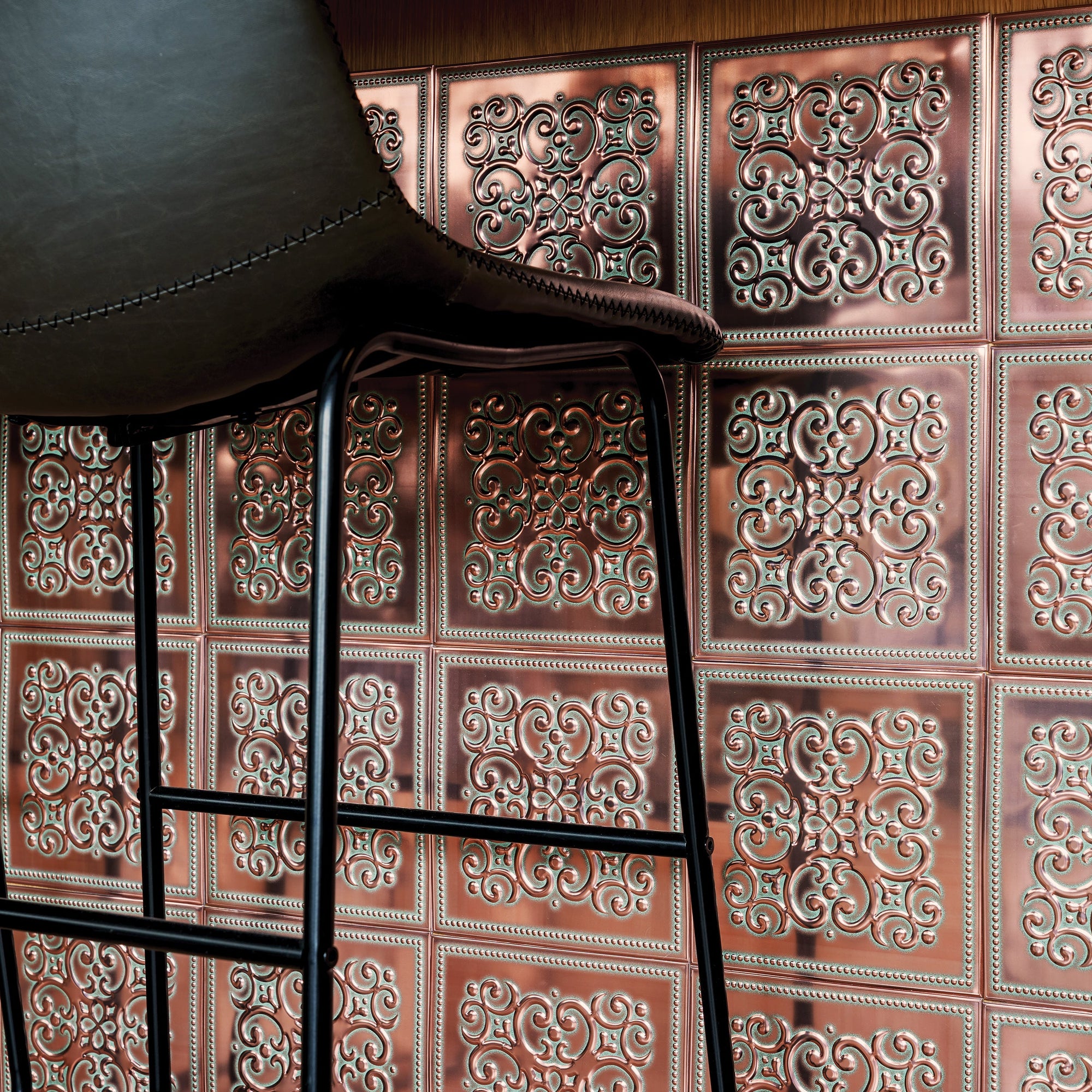 Rustic copper-finish embossed metal tiles covering a wall behind a black leather bar stool