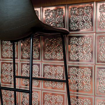 Rustic copper-finish embossed metal tiles covering a wall behind a black leather bar stool