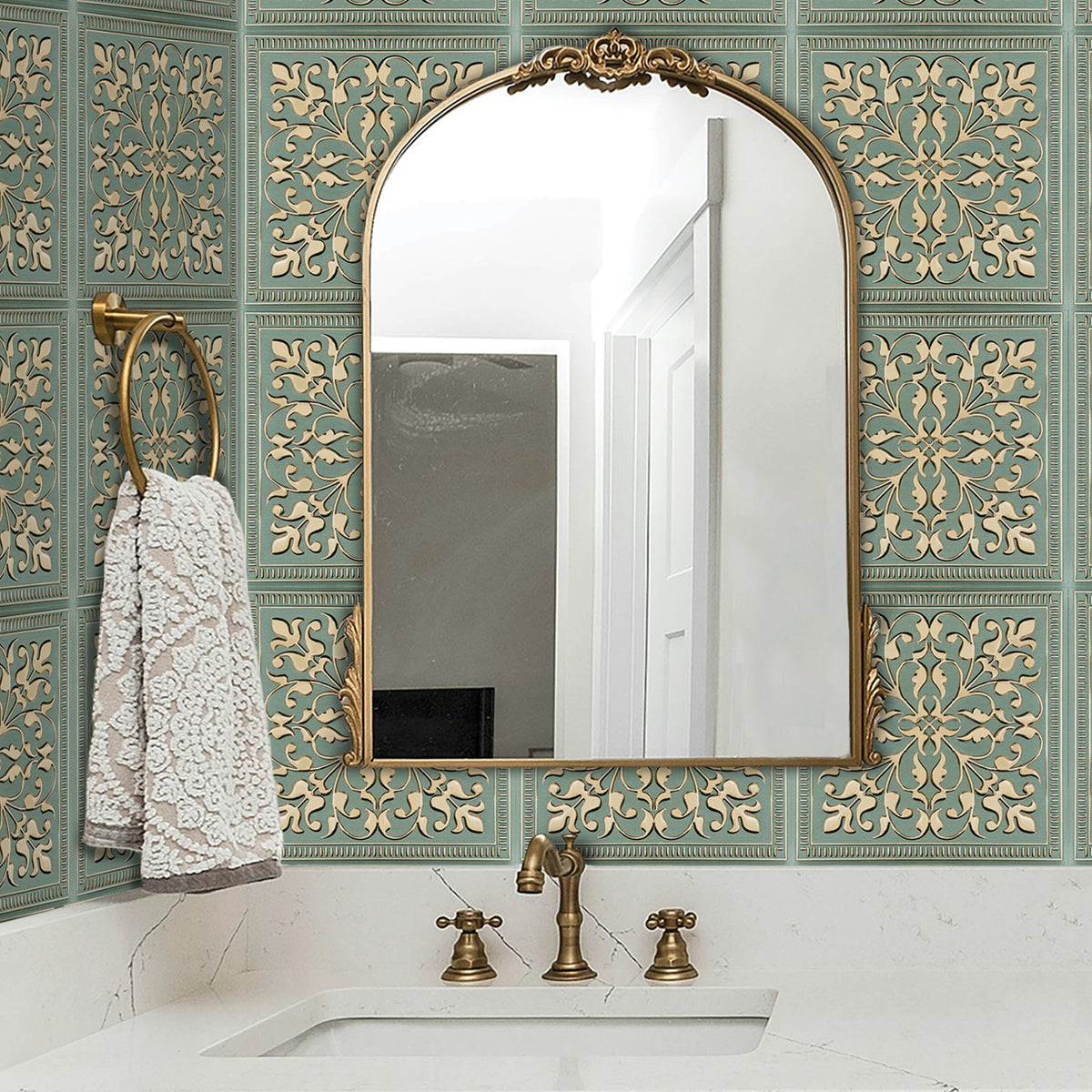 Vanity backsplash in sage green metal tile with raised cream and gold scrollwork, behind an undermount sink, antique brass faucet and an arched brass-framed mirror