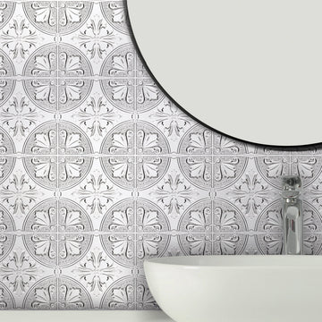 Silver Fleur embossed metal tiles on a bathroom wall behind a white vessel basin with a chrome faucet and a round black-rimmed mirror