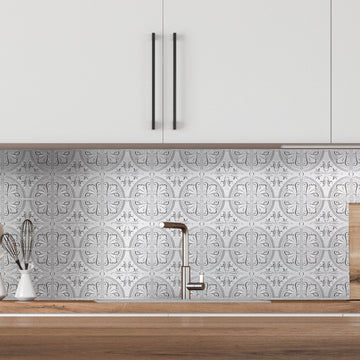Silver Fleur metal tiles covering a kitchen wall from a wood countertop up to white upper cabinets, behind a faucet and a crock of whisks