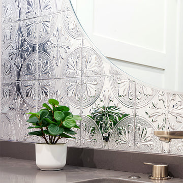 Silver Fleur peel and stick metal tile installed as a backsplash behind a round bathroom mirror, the kind of finish you can remove cleanly later.