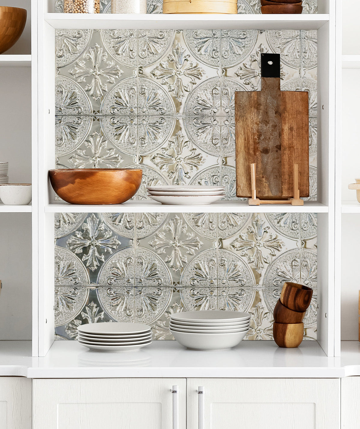 Silver fleur-de-lis metal tiles lining white open kitchen shelves with wooden bowls, white plates and a cutting board