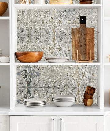 Silver fleur-de-lis metal tiles lining white open kitchen shelves with wooden bowls, white plates and a cutting board