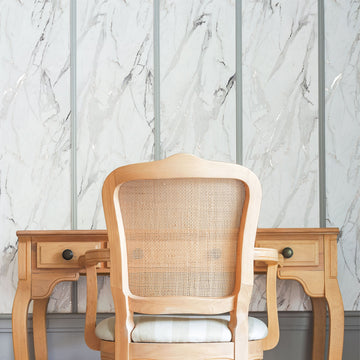 Marble-look peel and stick wall panels in vertical sections behind a wooden console table and cane-back chair.
