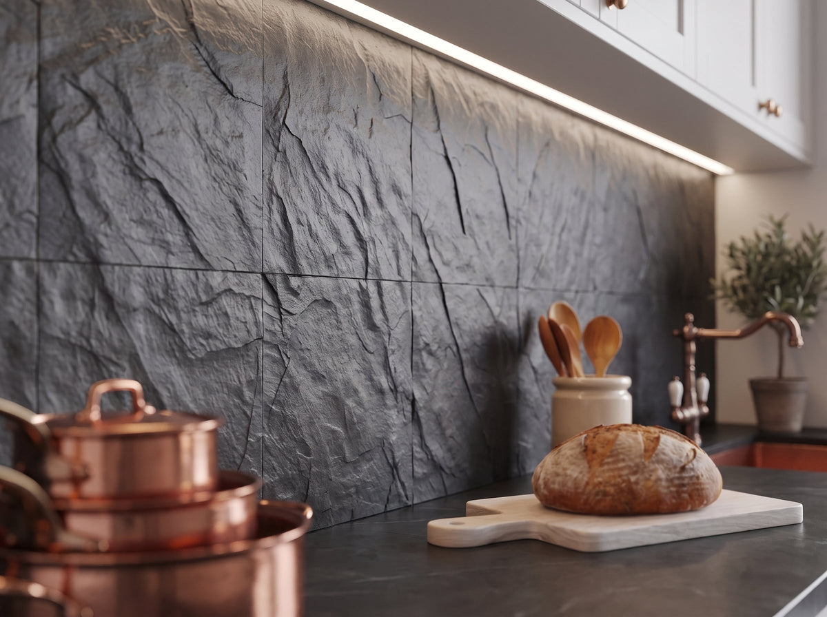 Dark charcoal stone-look backsplash with a rough split-face texture under cabinet lighting, with copper pans, a loaf of bread on a cutting board and wooden spoons on the counter